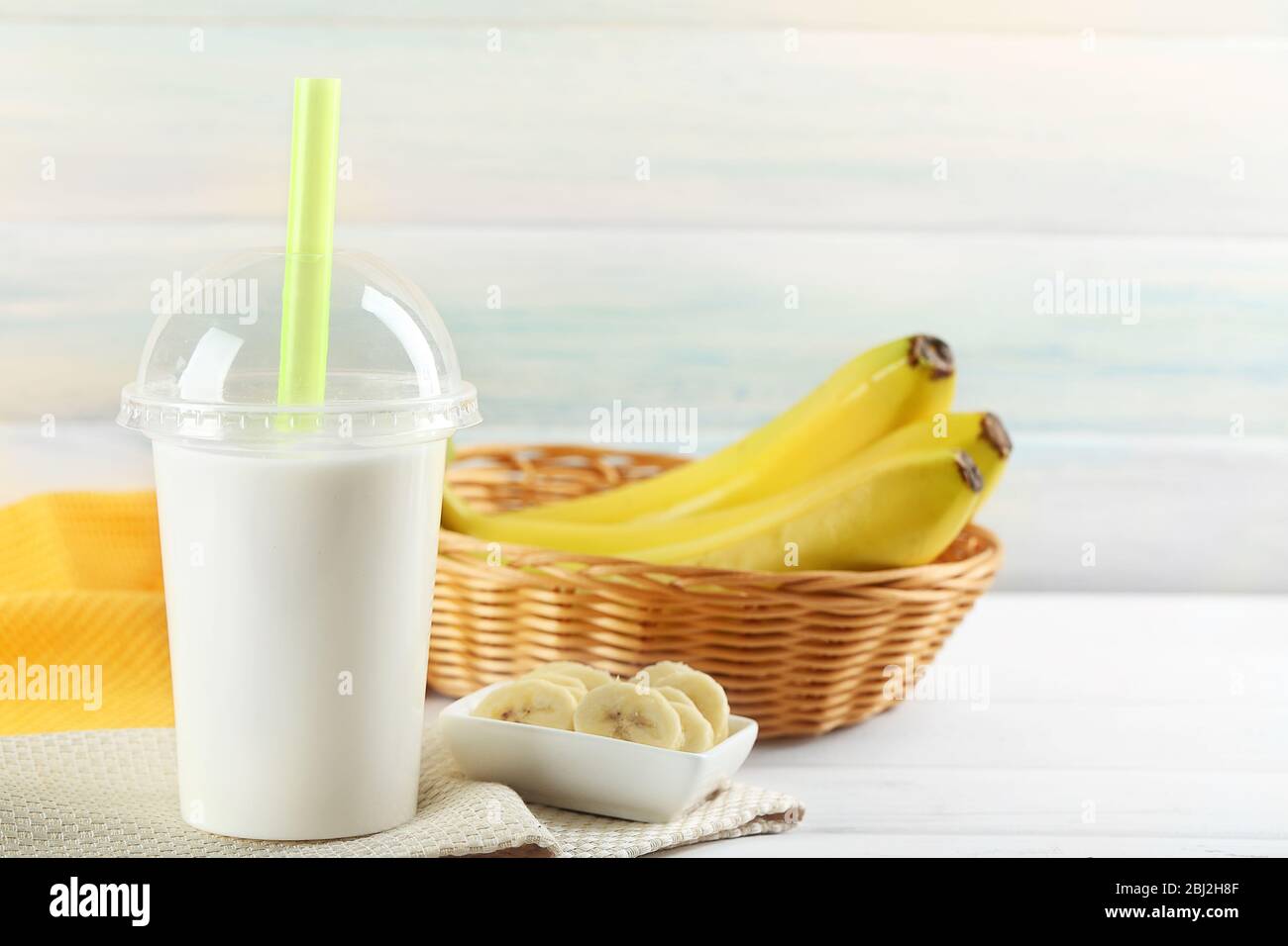 https://c8.alamy.com/comp/2BJ2H8F/plastic-cup-of-milkshake-with-banana-on-color-wooden-background-2BJ2H8F.jpg