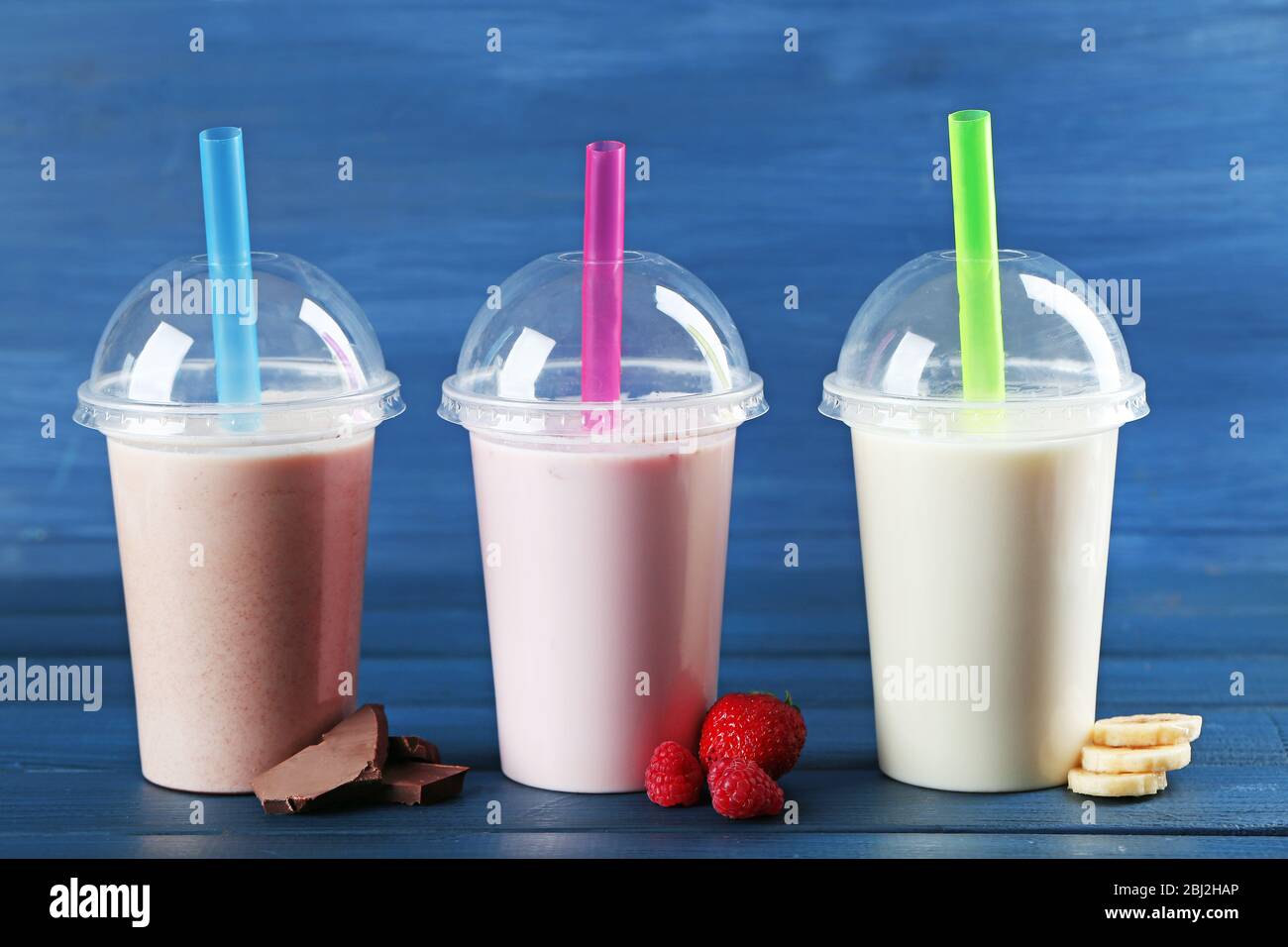 https://c8.alamy.com/comp/2BJ2HAP/plastic-cups-of-milkshake-on-color-wooden-background-2BJ2HAP.jpg