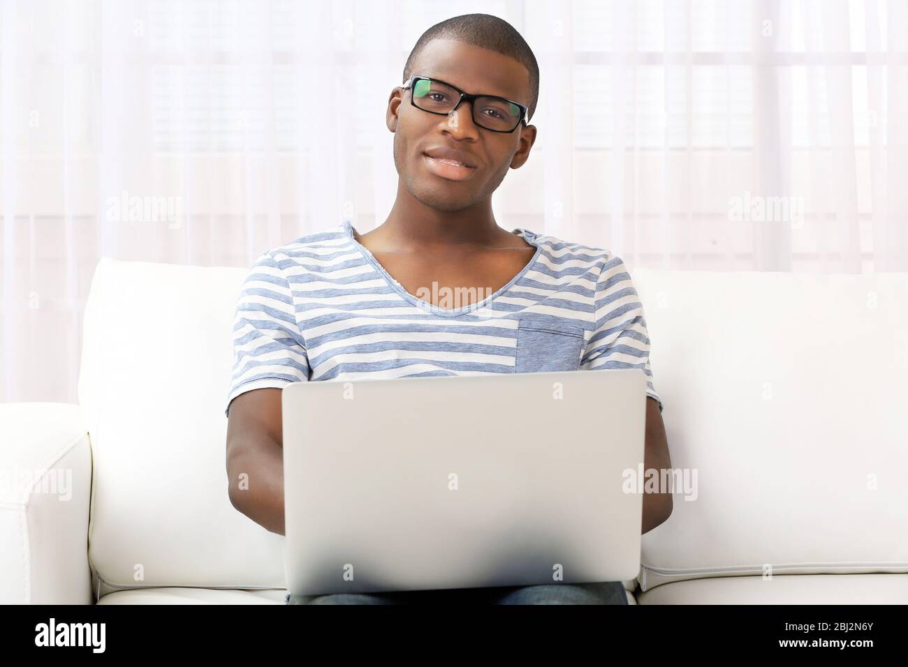 Handsome African American man sitting with laptop on sofa in room Stock ...