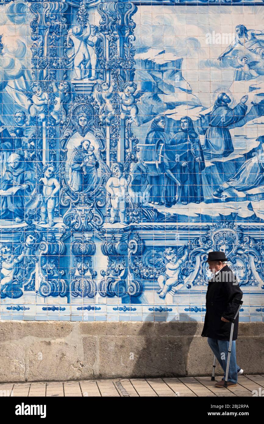 Man with walking cane passes azulejos Portuguese blue and white wall tiles of Capela das Almas de Santa Catarina  - St Catherine's Chapel in Porto, Po Stock Photo