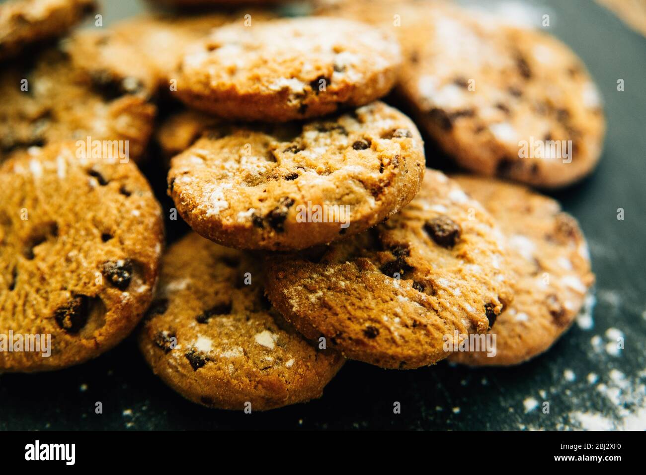 Close up of homemade chocolate chip cookies/biscuits sprinkled with flour on slate Stock Photo