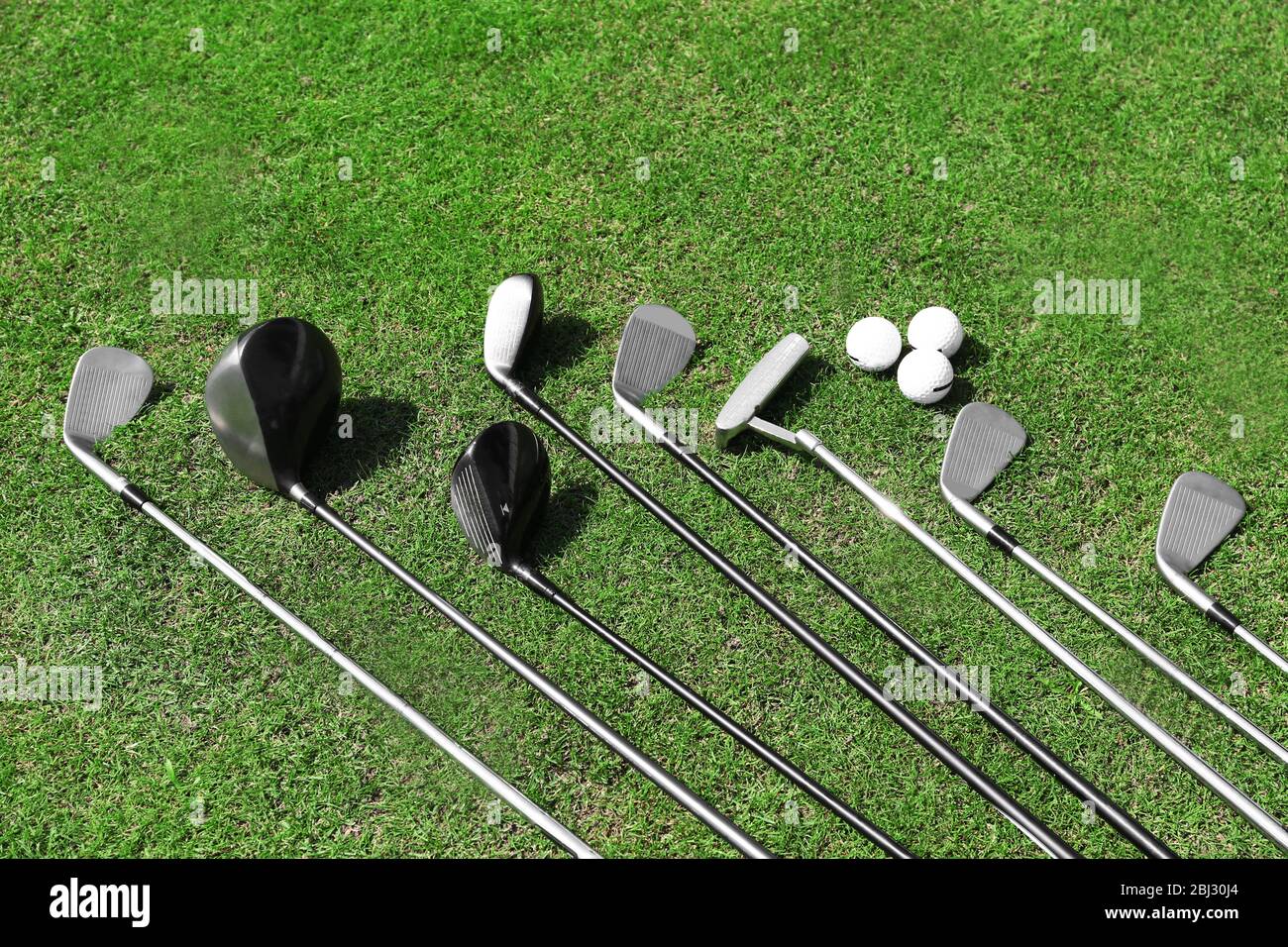 Different golf clubs in a row and balls on a green grass Stock Photo