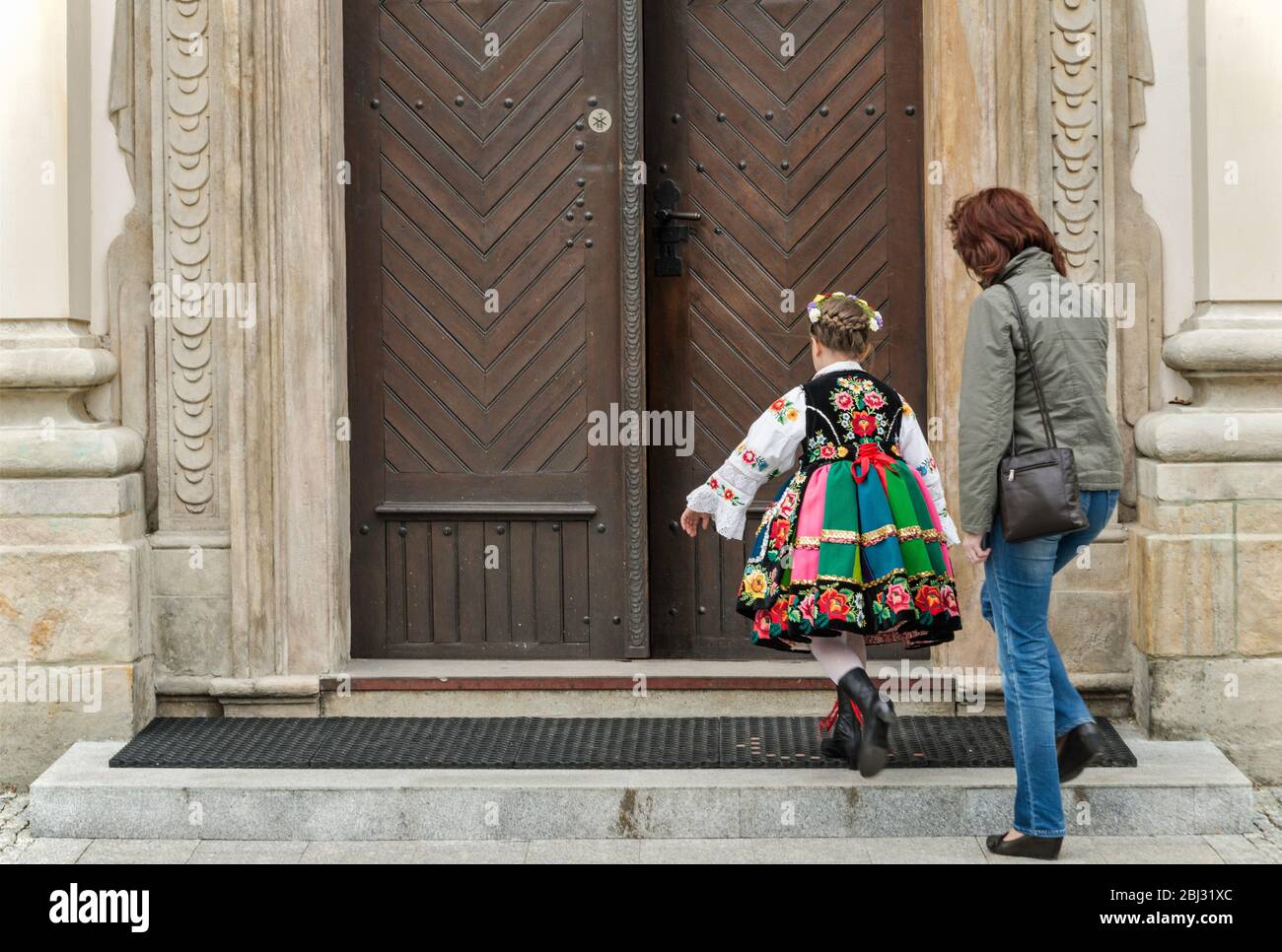 Girl wearing folk costume, mother, entering church for First Holy Communion event, Cathedral Basilica in Lowicz, Mazovia, Poland Stock Photo