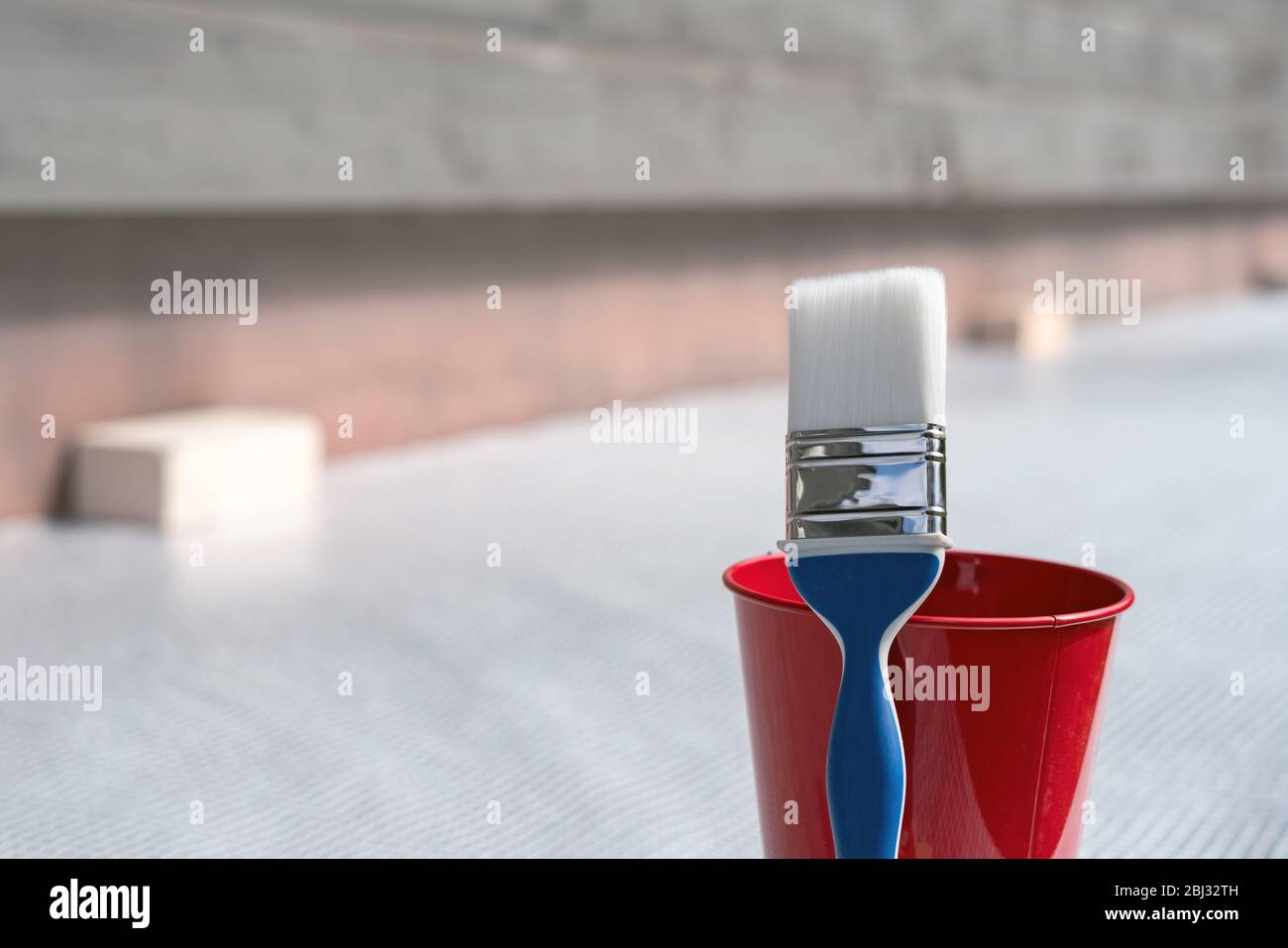 Paint brush and a bucket with paint next to a building exterior wall