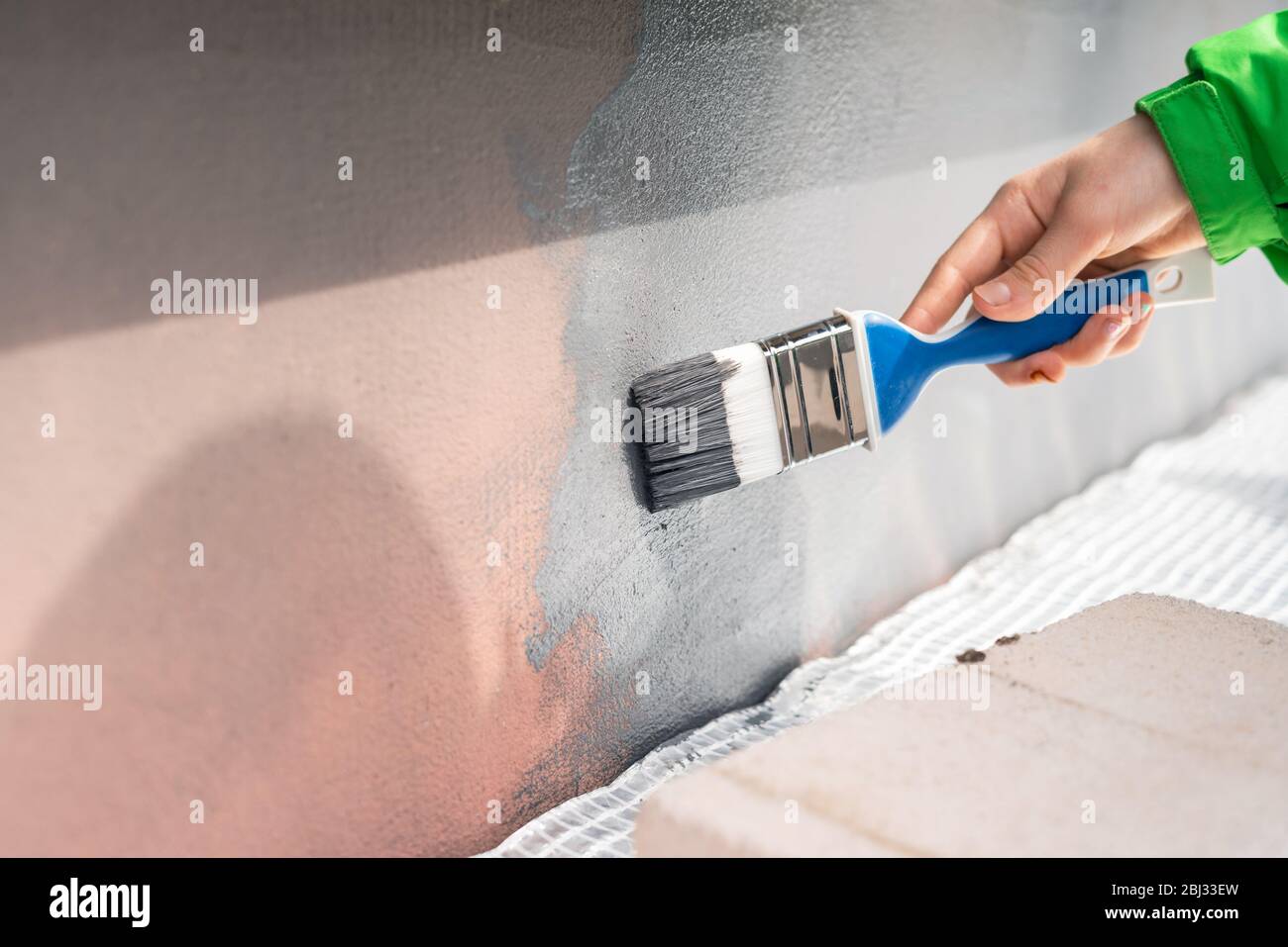 Closeup of hand with paint brush painting building exterior wall