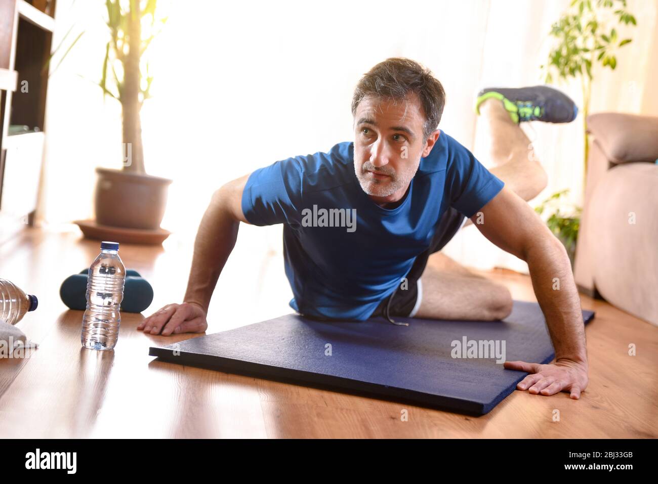 Man doing leg exercises lying on mat in his living room with water and