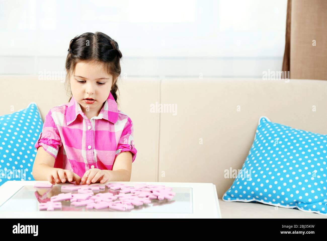 Cute little girl playing with puzzles on home interior background Stock ...