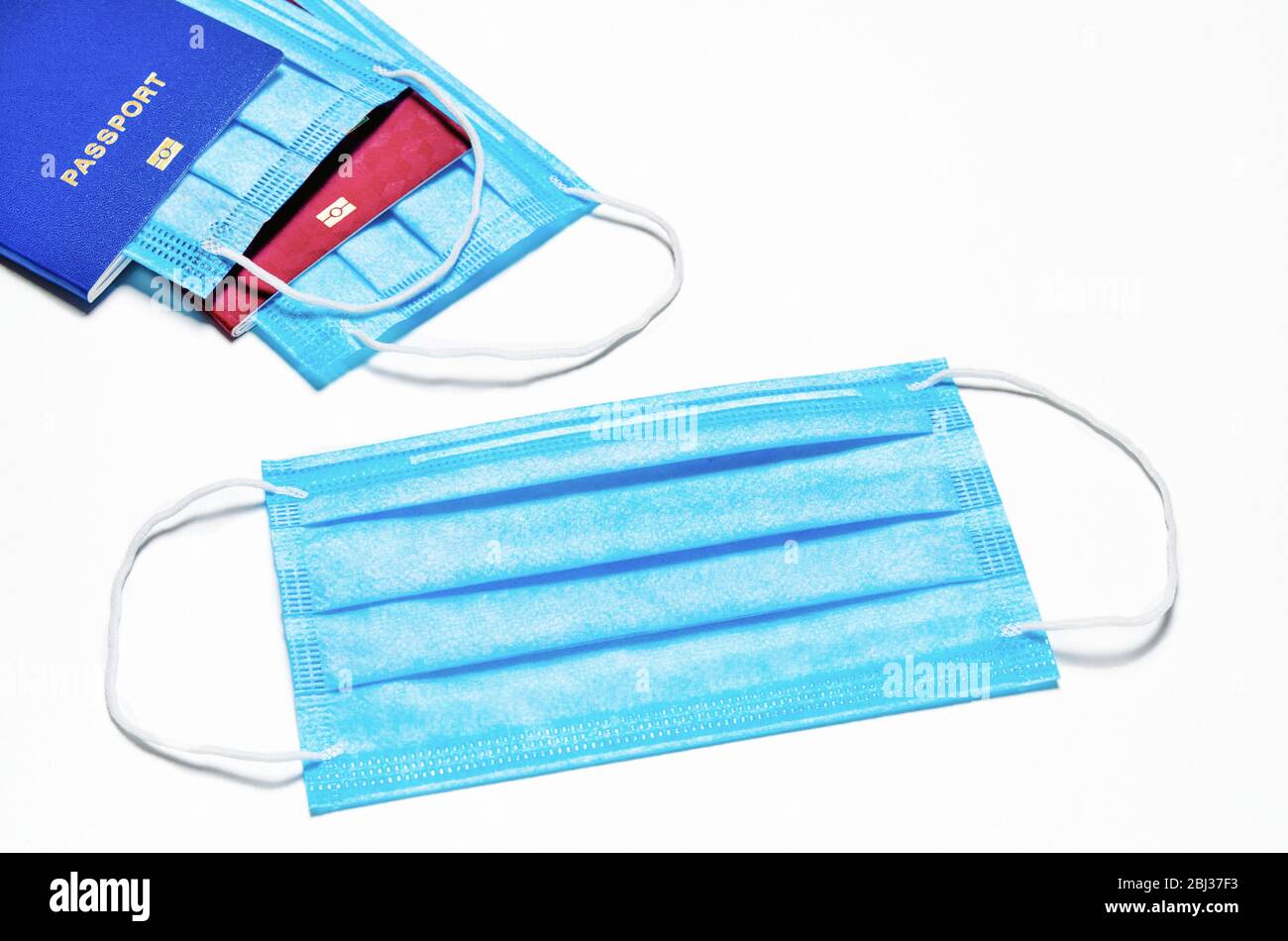 blue medical facial mask lies on a white background. in the background are two foreign passports of blue and red color with nested masks. world quaran Stock Photo