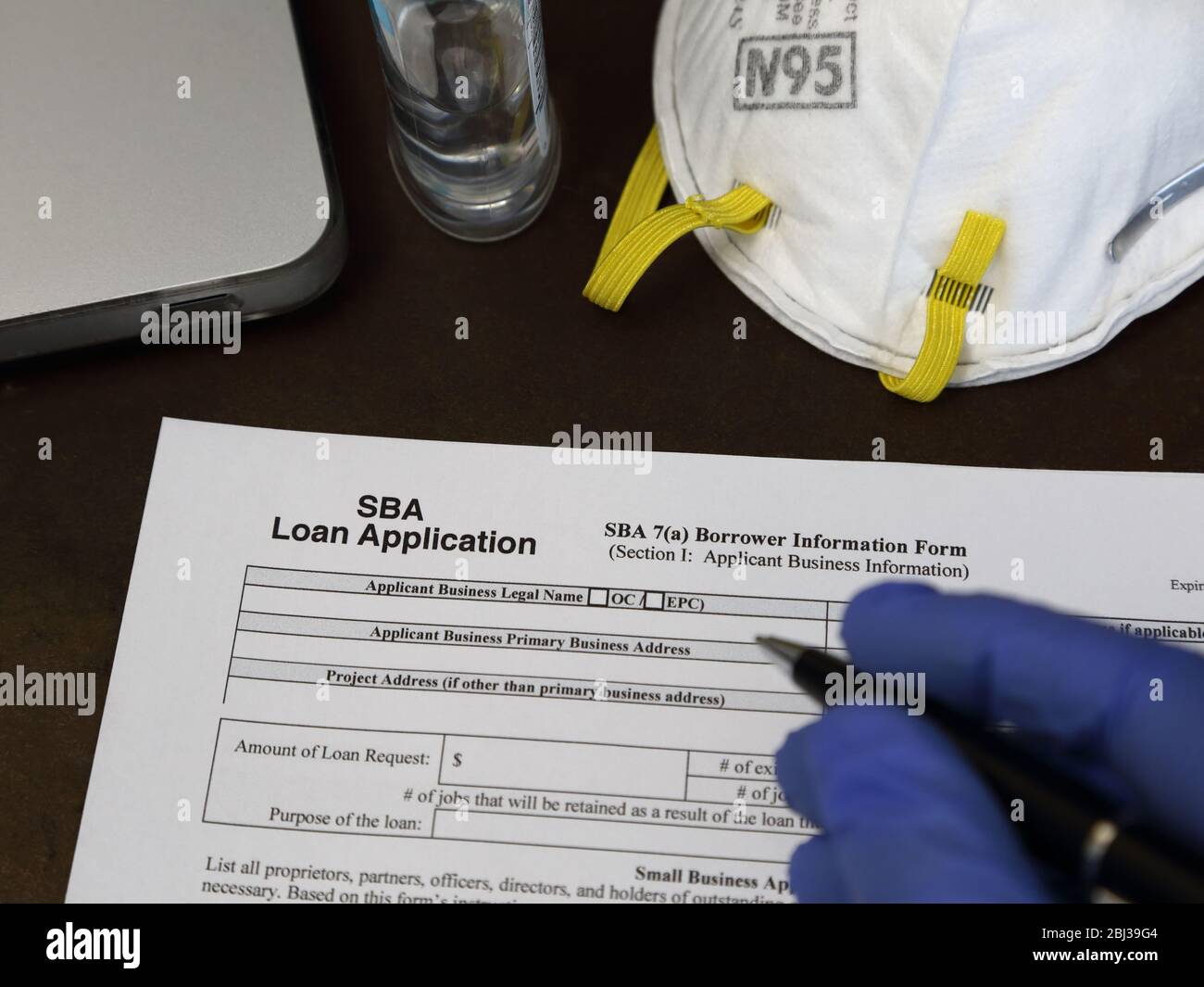 A rubber gloved hand is about to fill out a Small Business Administration aka SBA loan application form, with an N95 respirator dust mask nearby. Stock Photo