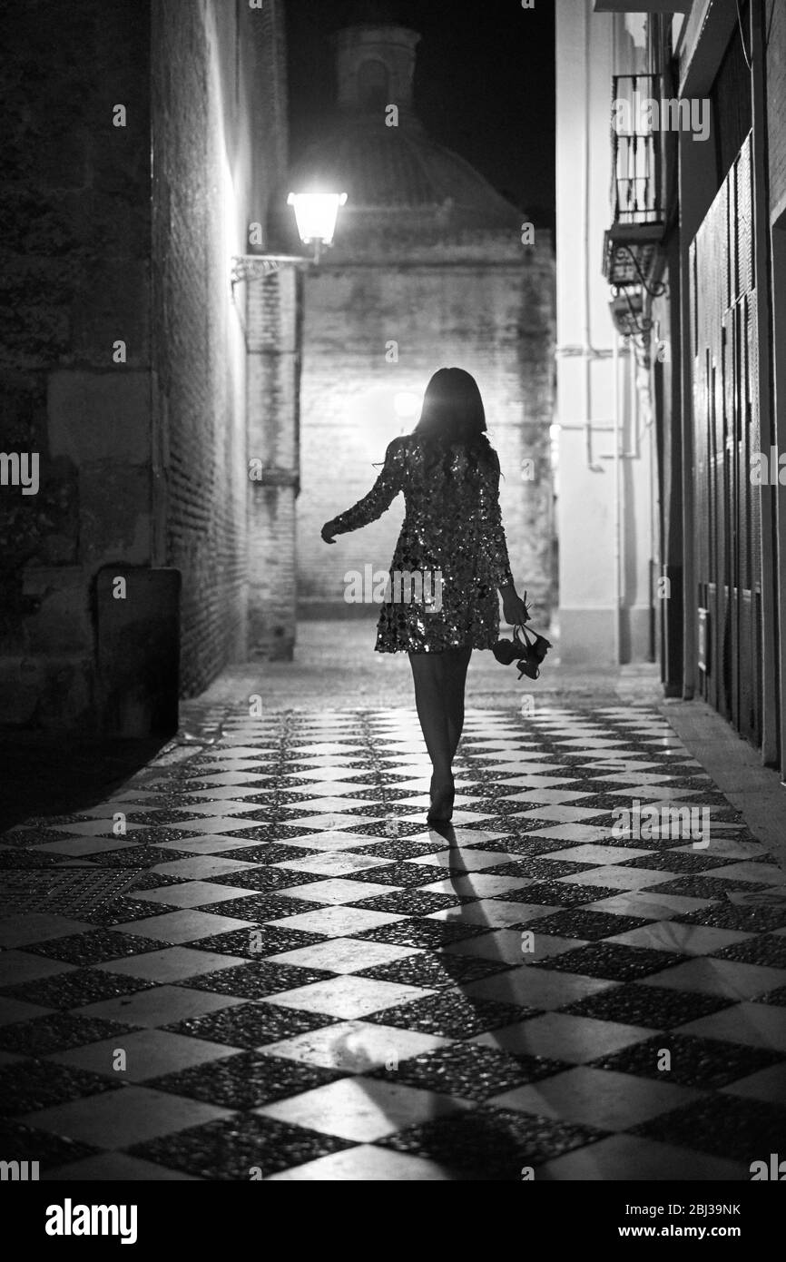 A young women walking down a cobbled street in Seville at night in a sequinned dress. Stock Photo