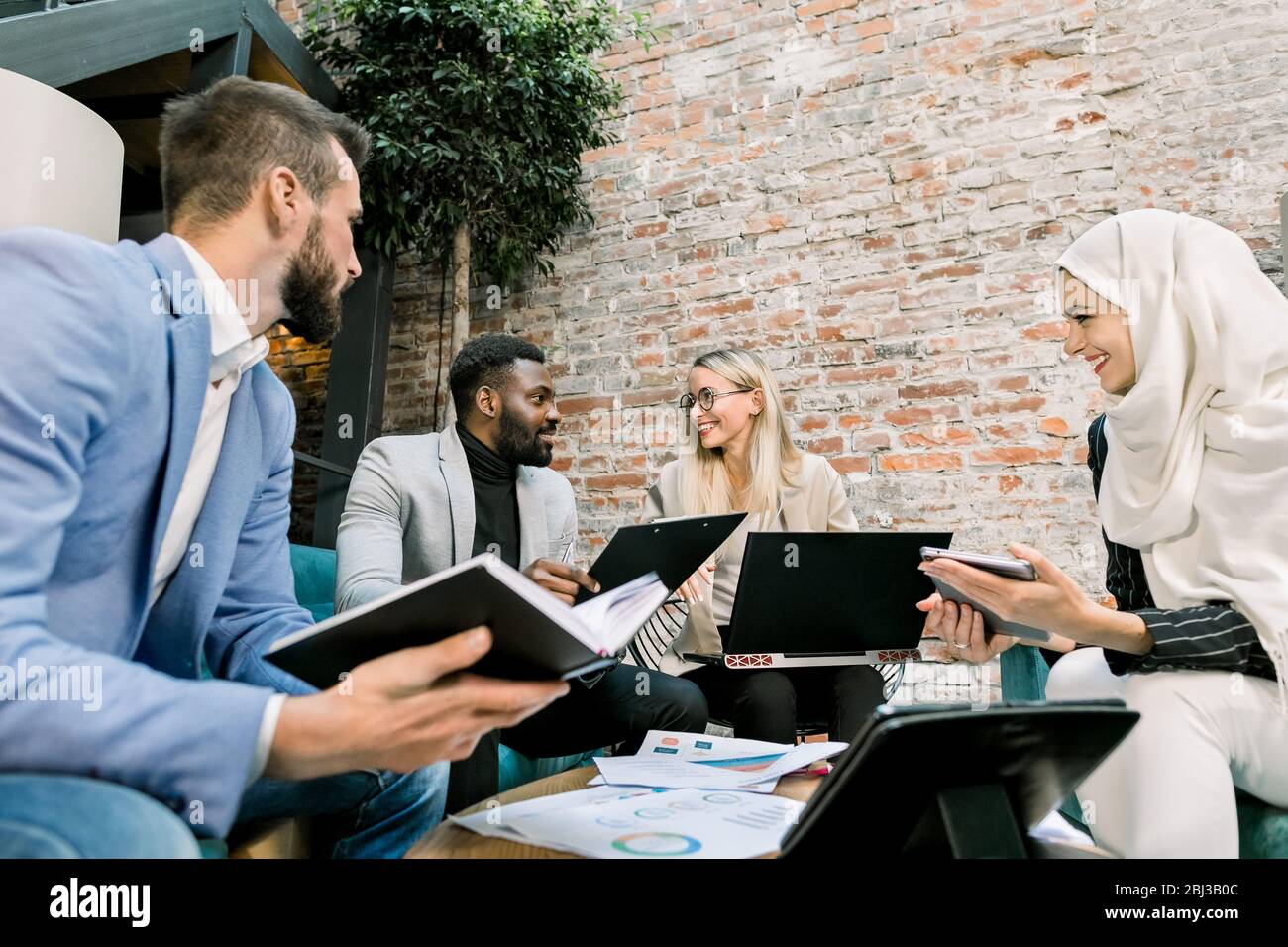 Four smiling young multiracial male and female business people sitting ...