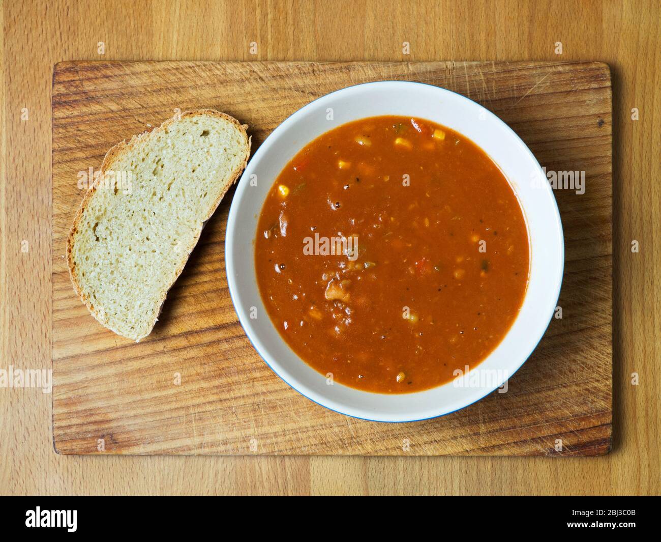 A bowl of three bean soup with a slice of homemade oat bread on a wooden bread board Stock Photo