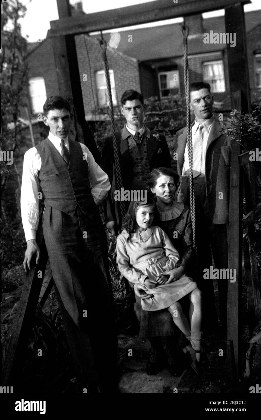 An unsmiling family pose for a photo in the garden of their Council house during the Depression of the 1930s Stock Photo