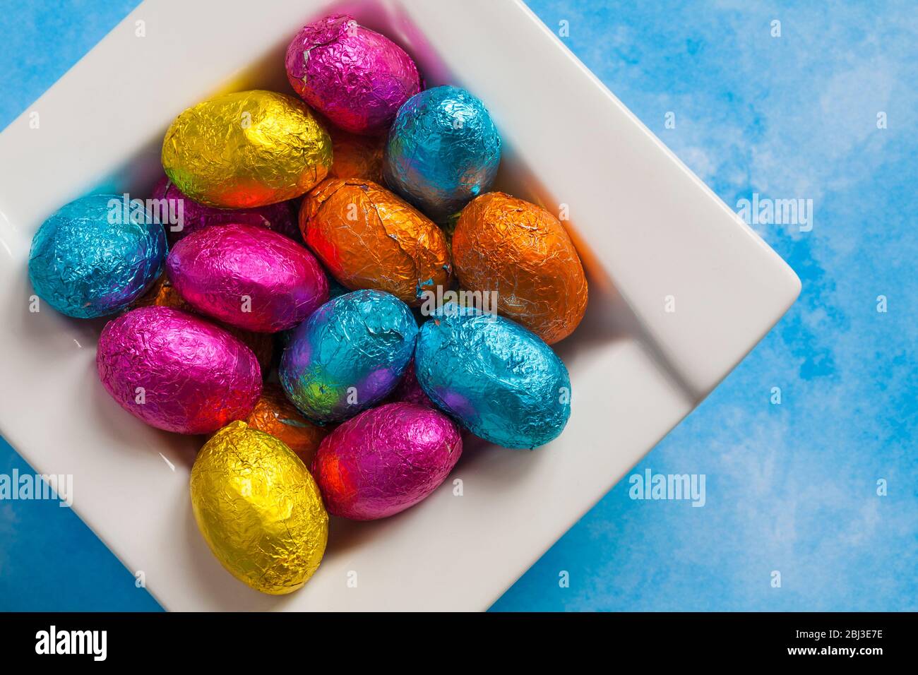 solid milk chocolate mini Easter eggs foil wrapped in bowl on blue