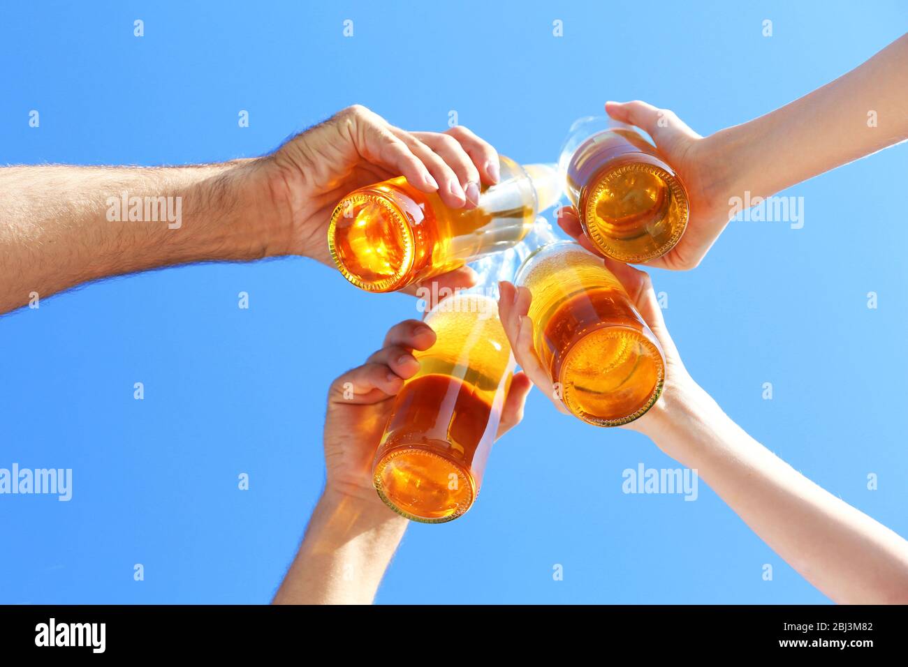 Bottles of beer in people's hands on blue sky background Stock Photo ...