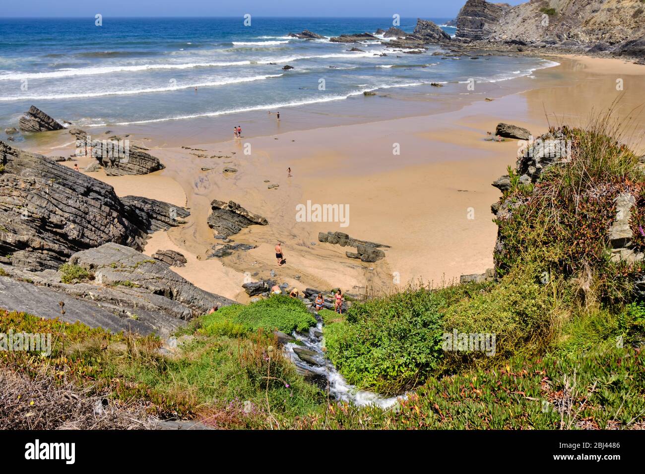 People play in the torrent that descends from the cliff at beach Praia do Carvalhal. Solo Backpacker Trekking on the Rota Vicentina and Fishermen's Tr Stock Photo