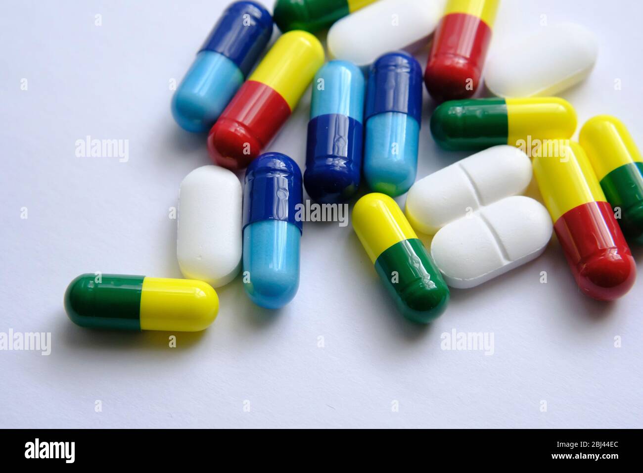 Pile of pills of different colours: blue, yellow, red and white) placed on top of white paper. Illustrative for medical, health and other subjects. Ma Stock Photo