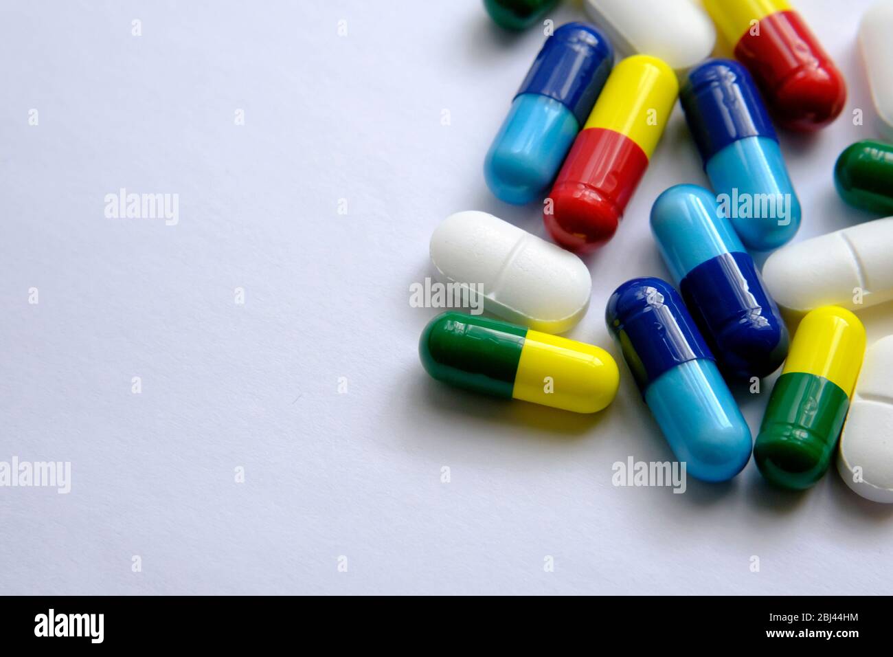 Pile of pills of different colours: blue, yellow, red and white) placed on top of white paper. Illustrative for medical, health and other subjects. Ma Stock Photo