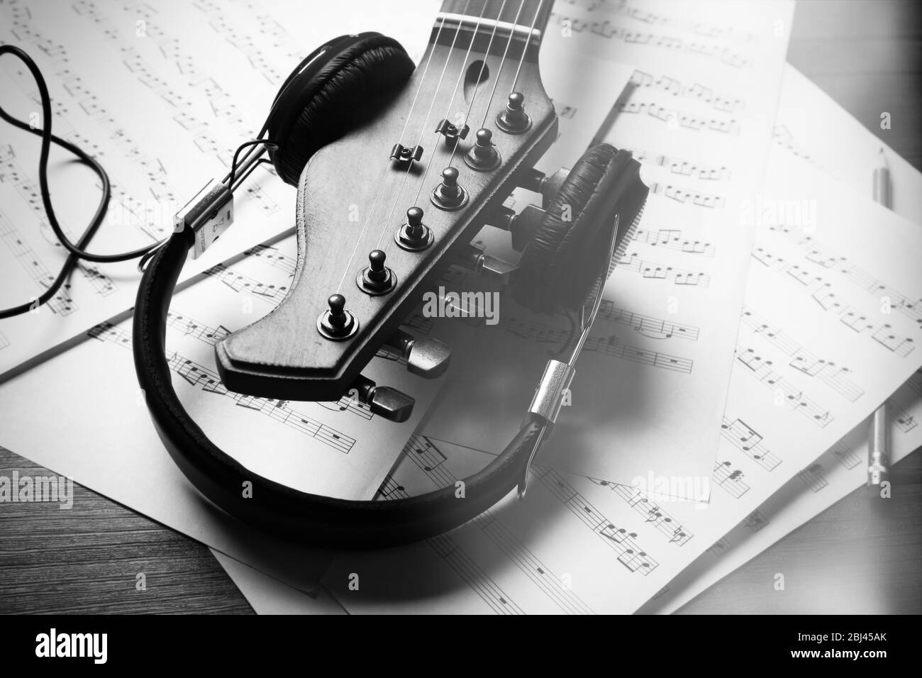 Neck of acoustic guitar with headphones and music notes on table, close
