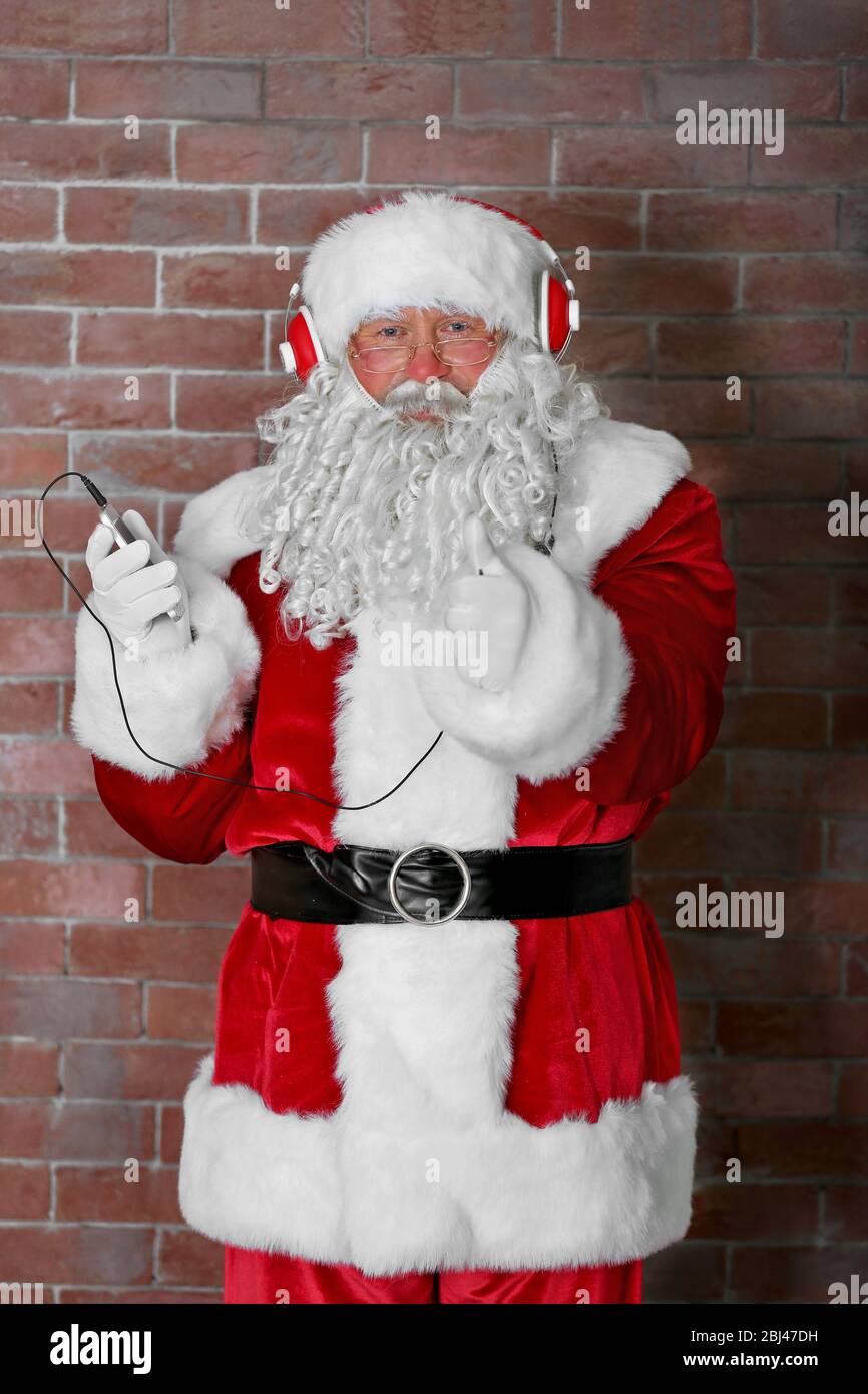 Santa Claus with headphones listening to music on brick wall background