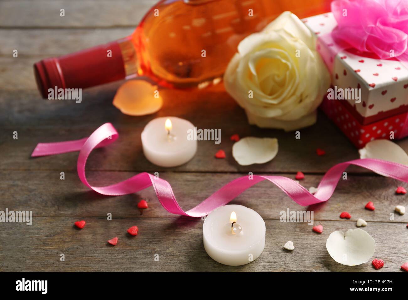 A bottle of wine, candles, a white rose and a gift in the box, on