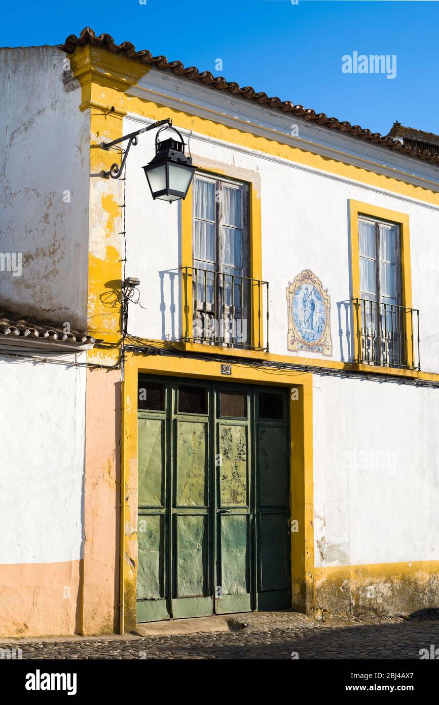 Typical white and yellow house with balcony, lantern, old front door and azulejo blue tiles of religious art in Evora, Portugal Stock Photo