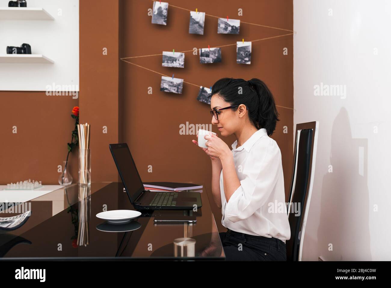 Young woman with glasses taking a coffee break while working in her makeshift home office. Work from home concept. Stock Photo