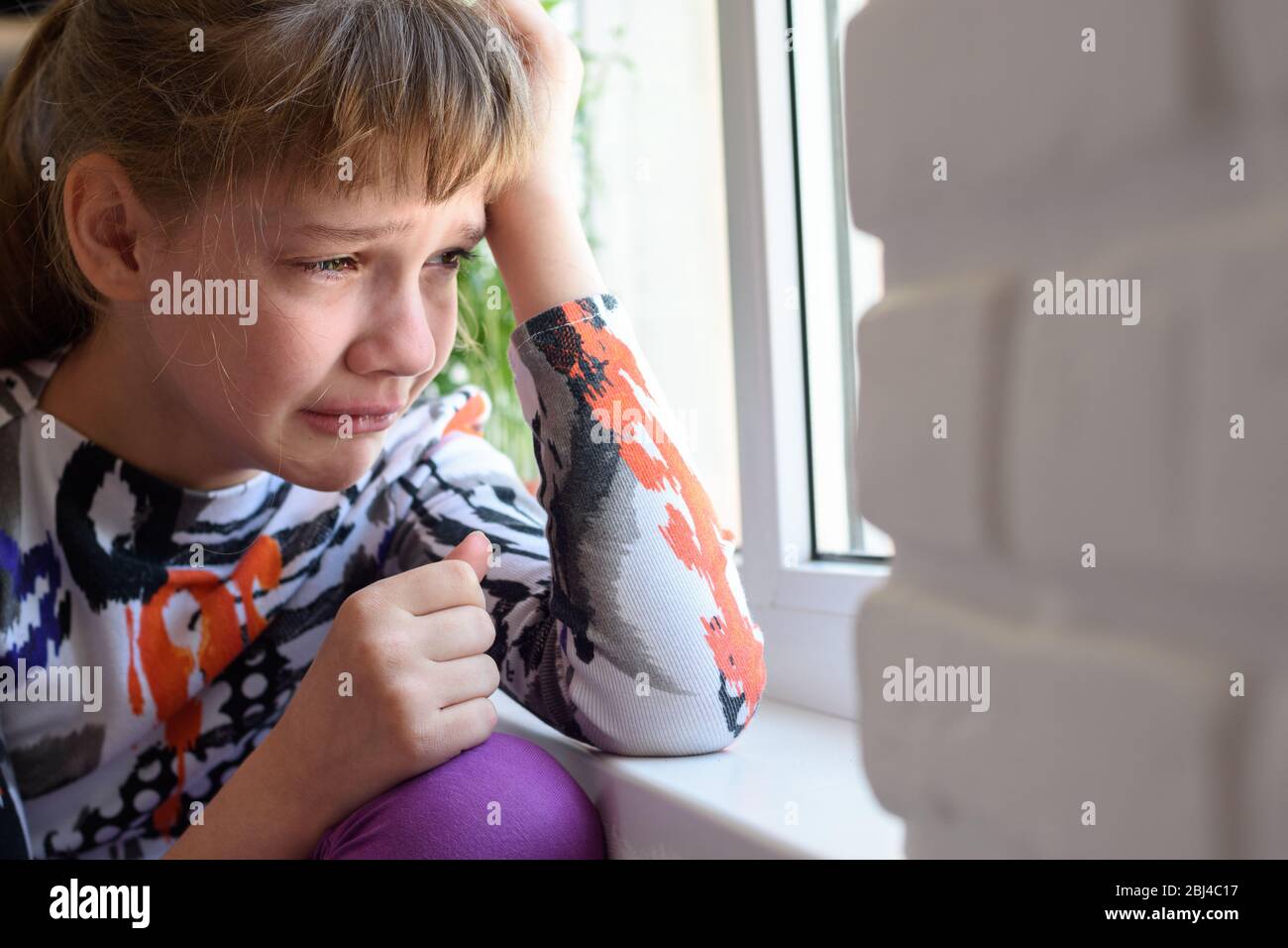 Upset girl crying sitting by the window Stock Photo