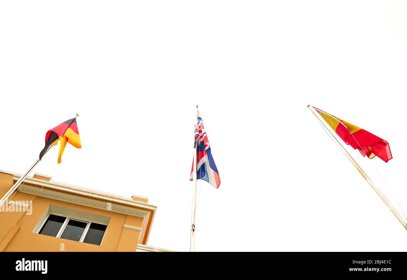 Three national flags: German, British and Spanish on flagpoles. Stock Photo