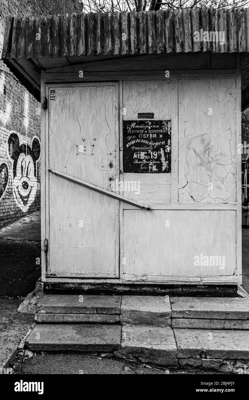 Black and white photo of old stall of shoe workshop with signboard near closed door. Architecture of European city. Retro building exterior. Doorway o Stock Photo