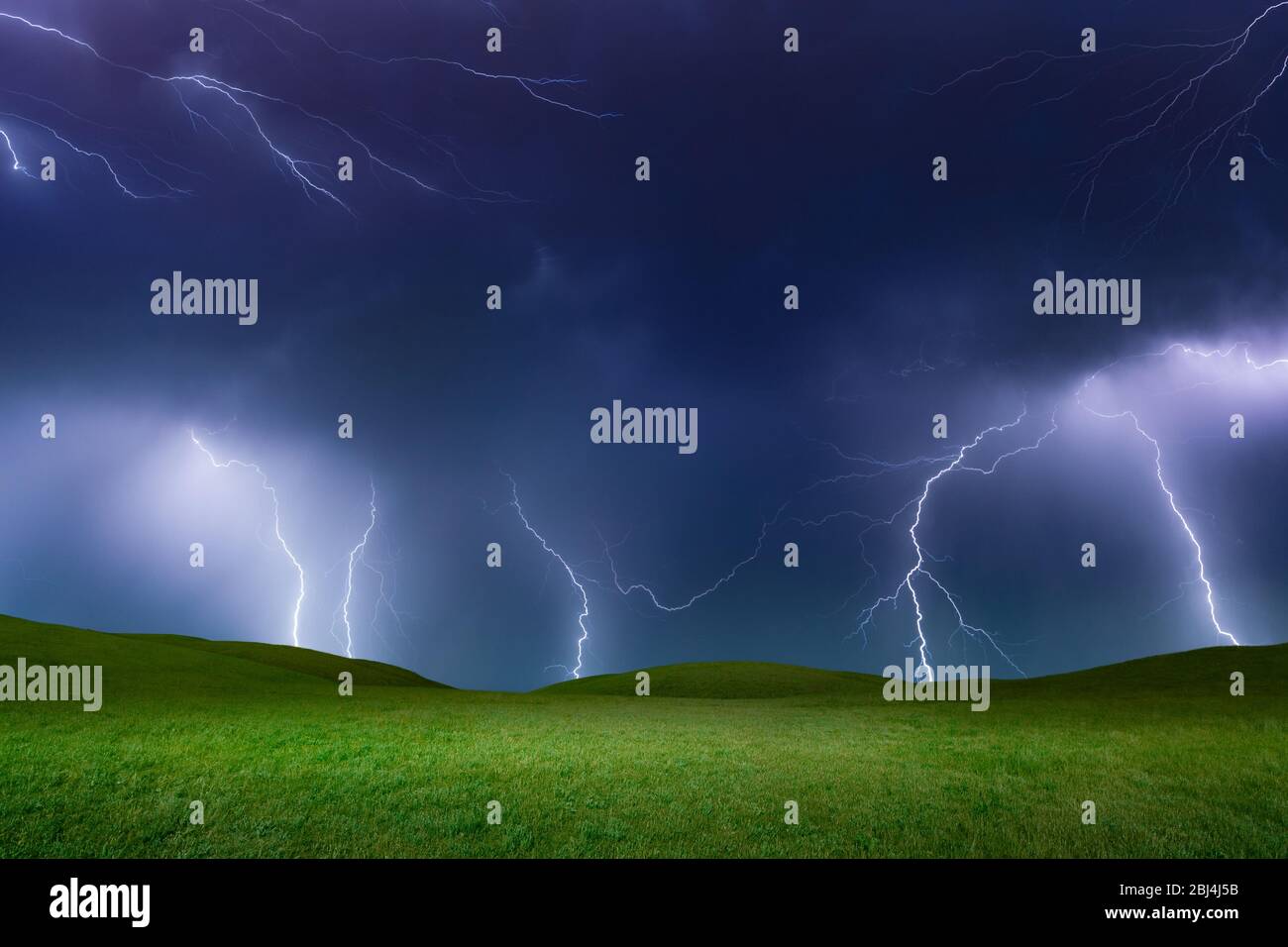 Powerful lightnings in dark stormy sky above green grass hills, weather ...