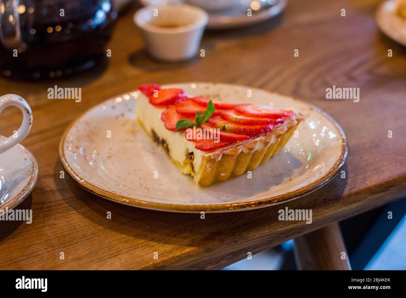 A piece of cheesecake with strawberries and mint leaves on a plate Stock Photo