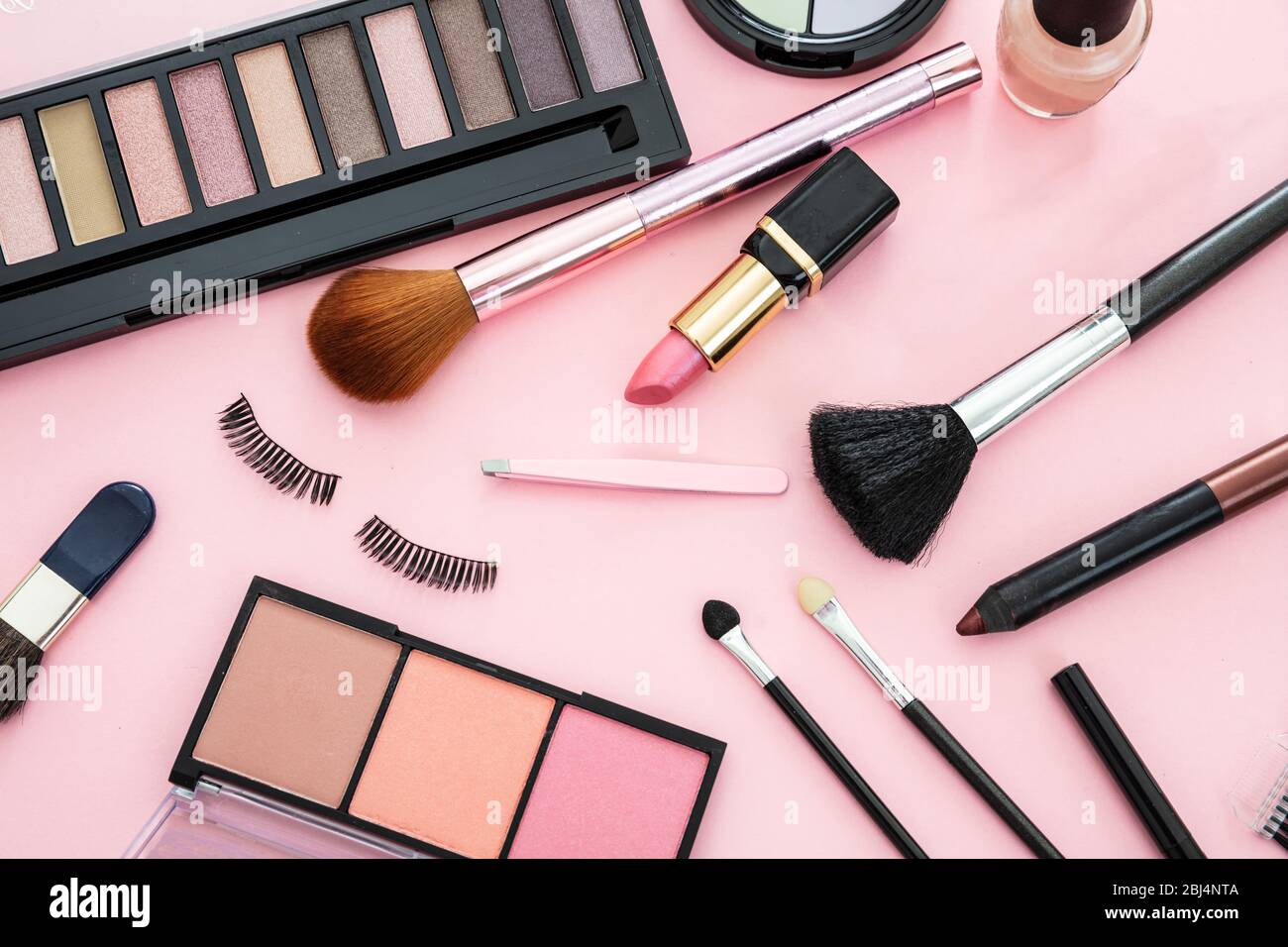 Make up cosmetics flat lay. Lipstick and nail polish, eye shadows and blush, brushes and pencils against pink color background Stock Photo