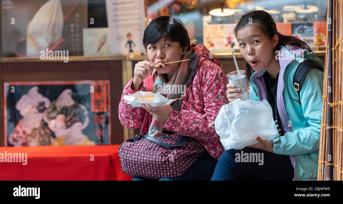 Two local women enjoy a local favorite, Yakitori, (grilled chicken or octopus on a skewer at the Nishiki food market in Kyoto, Japan Stock Photo