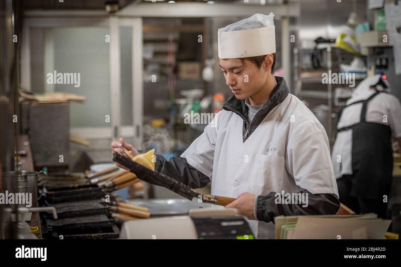 A seller at the Nishiki food market in Kyoto Japan offering and preparing food for sale Stock
