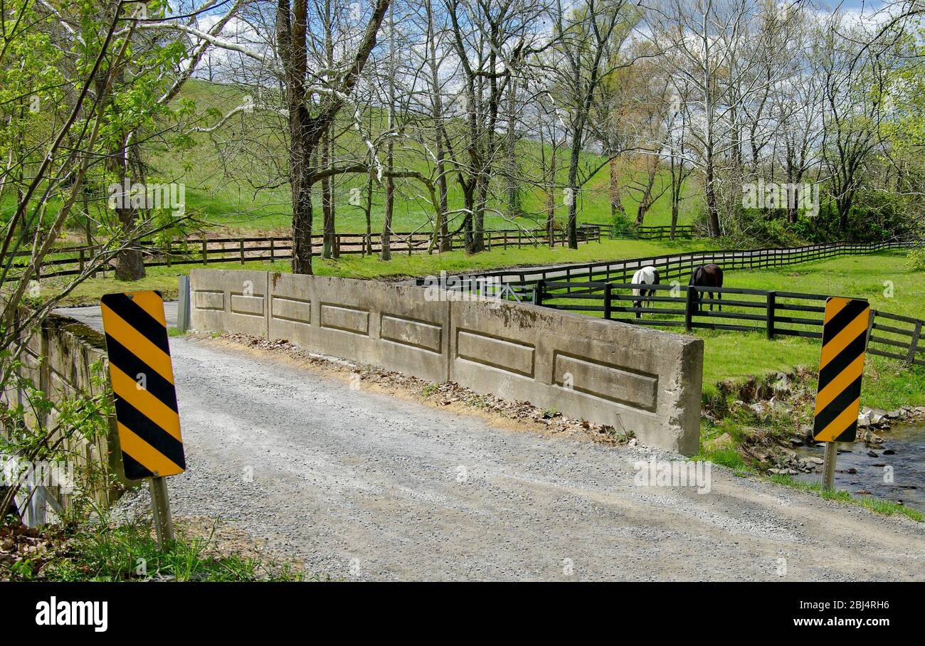 Small Country Bridge:  A narrow gravel road crosses a one lane bridge and passes beside a horse farm in western Virginia. Stock Photo