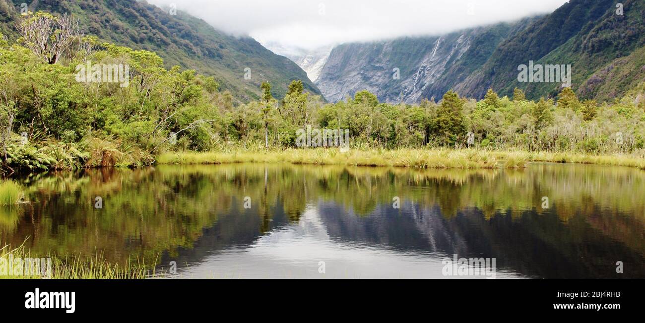 Panoramic view from the Peters Pool of the Franz Josef Glacier with great, perfectly symmetrical reflection in the water. Stock Photo