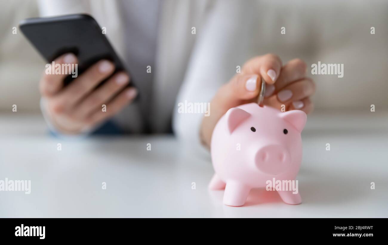 Woman saving money using smartphone and piggy bank Stock Photo