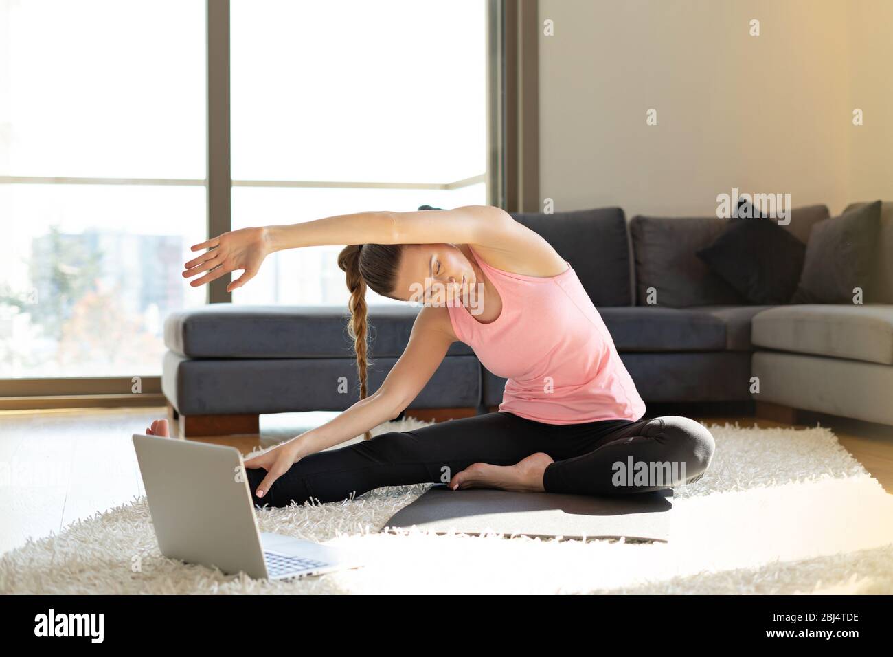 Online sport fitness yoga training. young woman and doing exercises on yoga mat opposite laptop with online master class. training at home Stock Photo