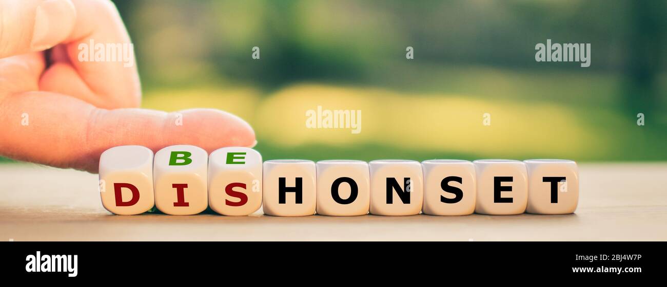 Hand turns dice and changes the expression 'dishonest' to 'be honest'. Stock Photo