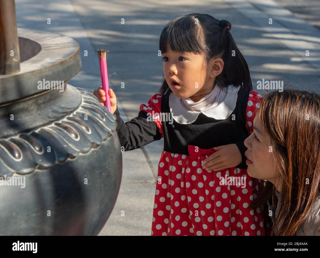 A child and her mother burn incense at the Shinobazu-no-ike Bentendo temple in ueno park in tokyo. Stock Photo