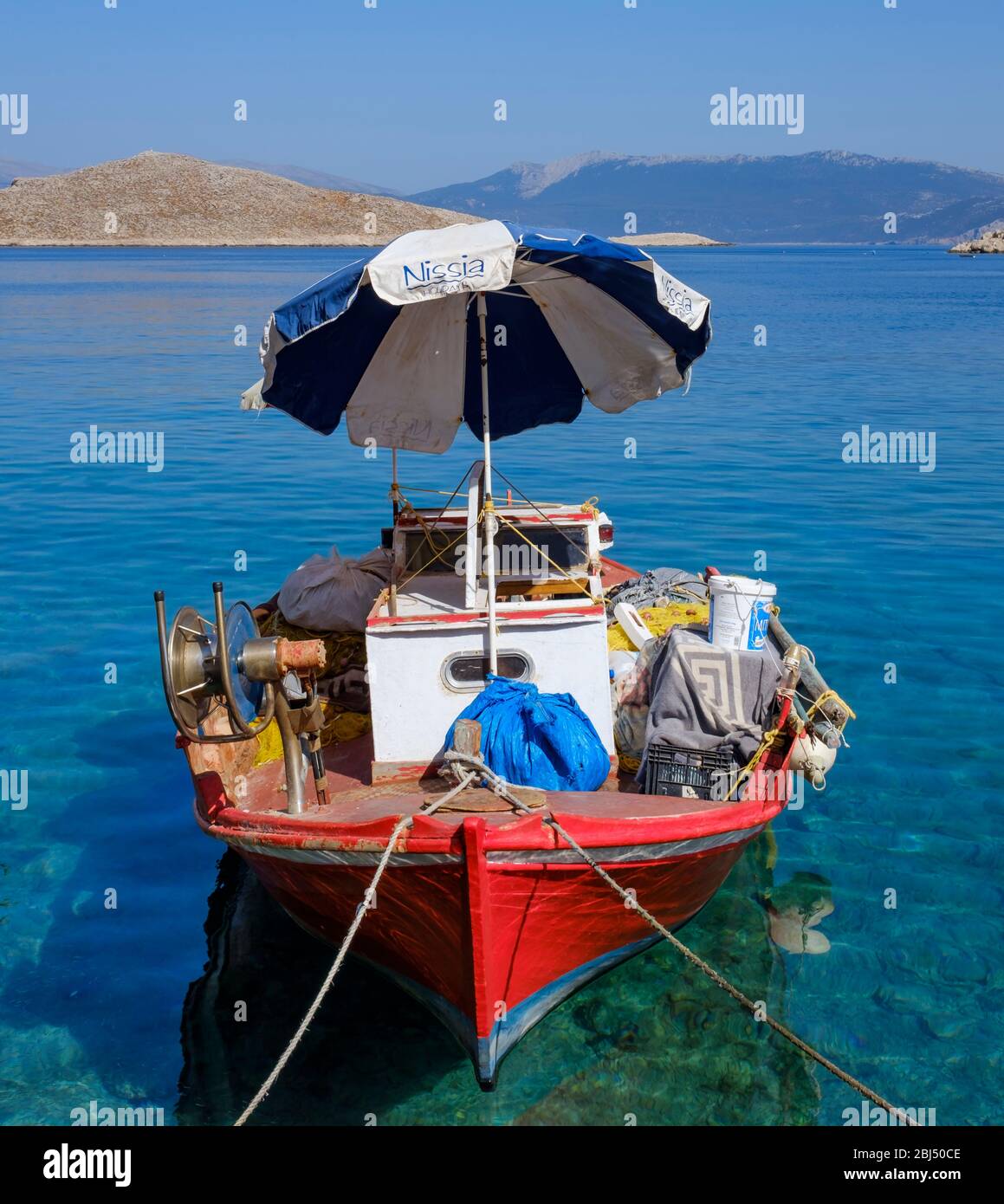 Red boat with a parasol in Halki harbor. Stock Photo