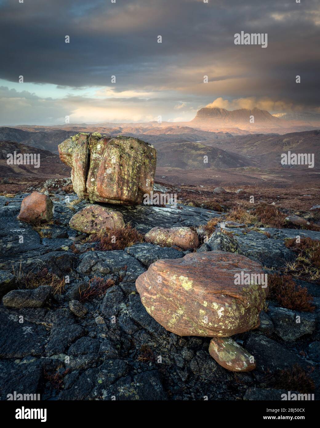 A collection of erratic boulders at the Aird of Coigach with Suilven in the background lit by the evening sun. Stock Photo