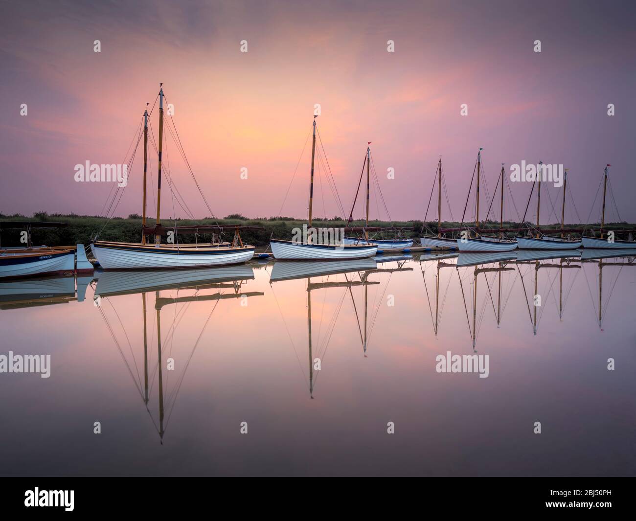 A line of identical sailing boats at dawn on a calm spring morning. Stock Photo
