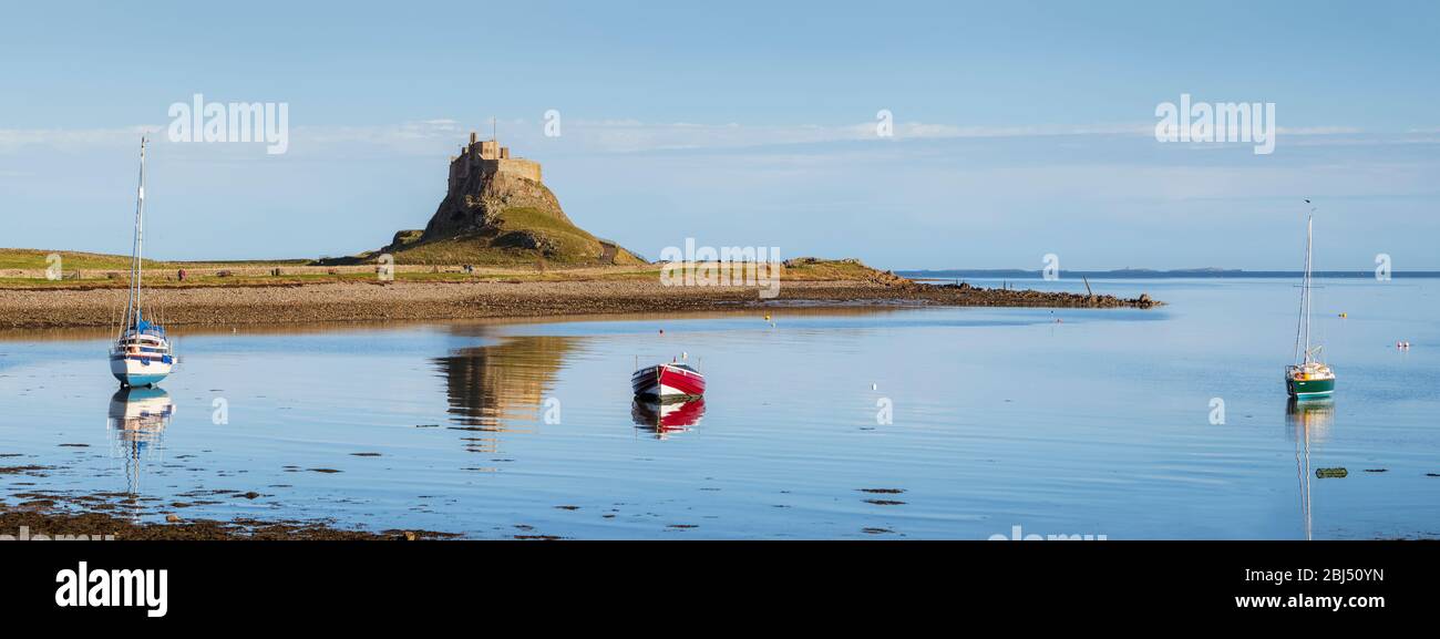 A panoramic image of the castle on Holy Island with boats in the foreground at high tide. Stock Photo