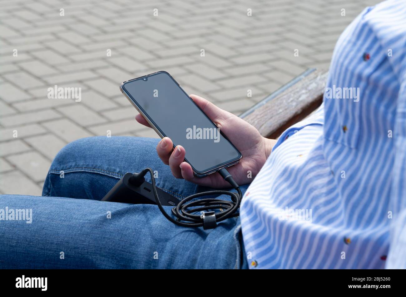 Girl on the bench uses phone while charging from the power bank. Modern technology concept. Selective focus Stock Photo
