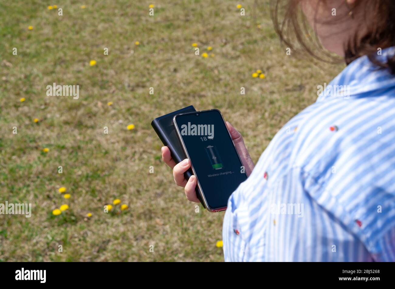 Girl charging smartphone without cable from induction power bank in the park. Modern technology concept. Selective focus Stock Photo
