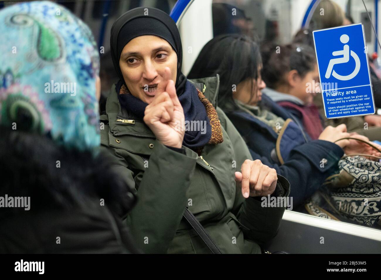 A woman wearing a headscarf and gesturing with her hands on the London Underground, England Stock Photo