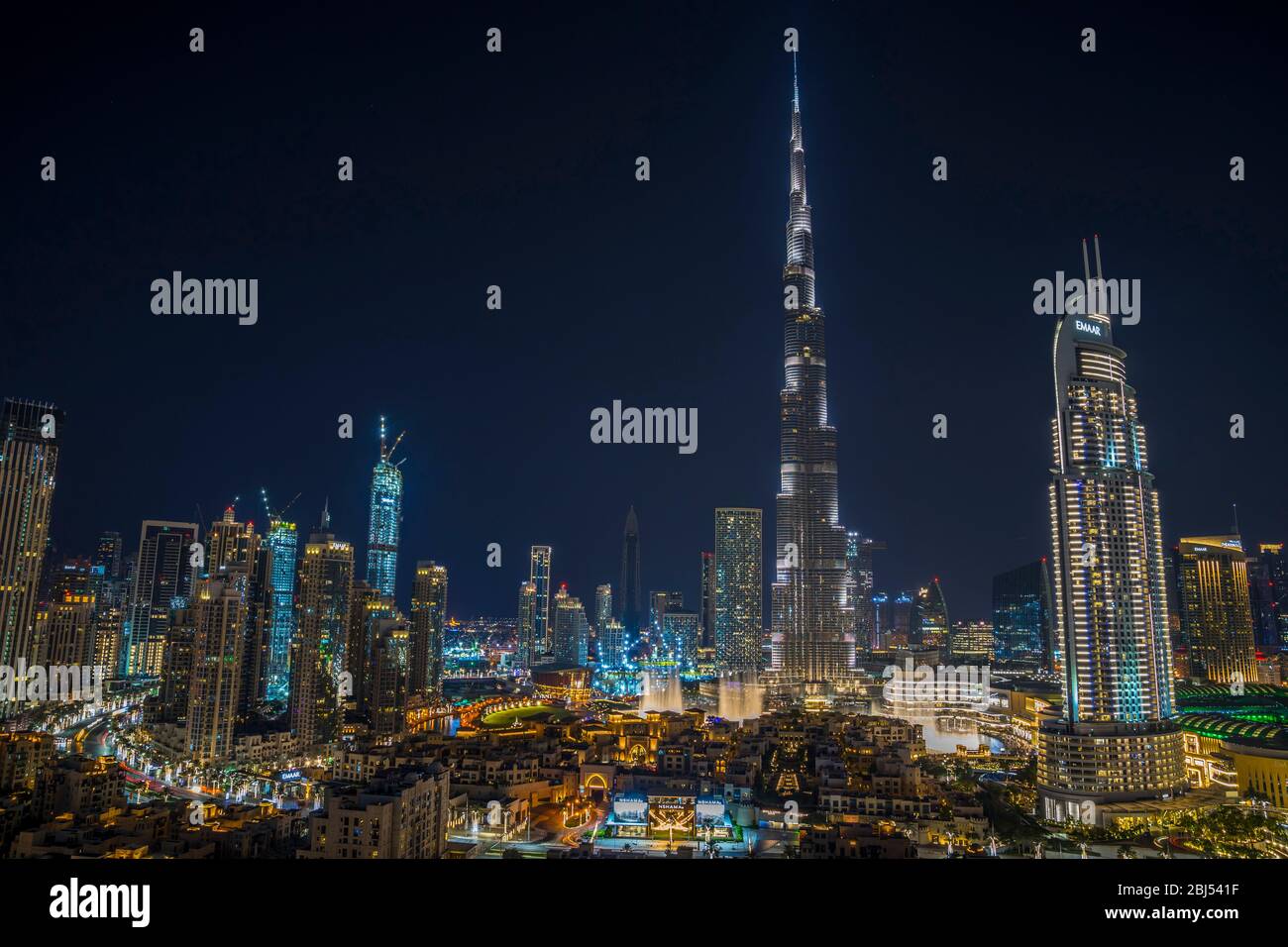 Dubai skyline at night as the waters of the fountain dance beneath the Burj Khalifa and the red glow of passing cars fill the streets. Stock Photo