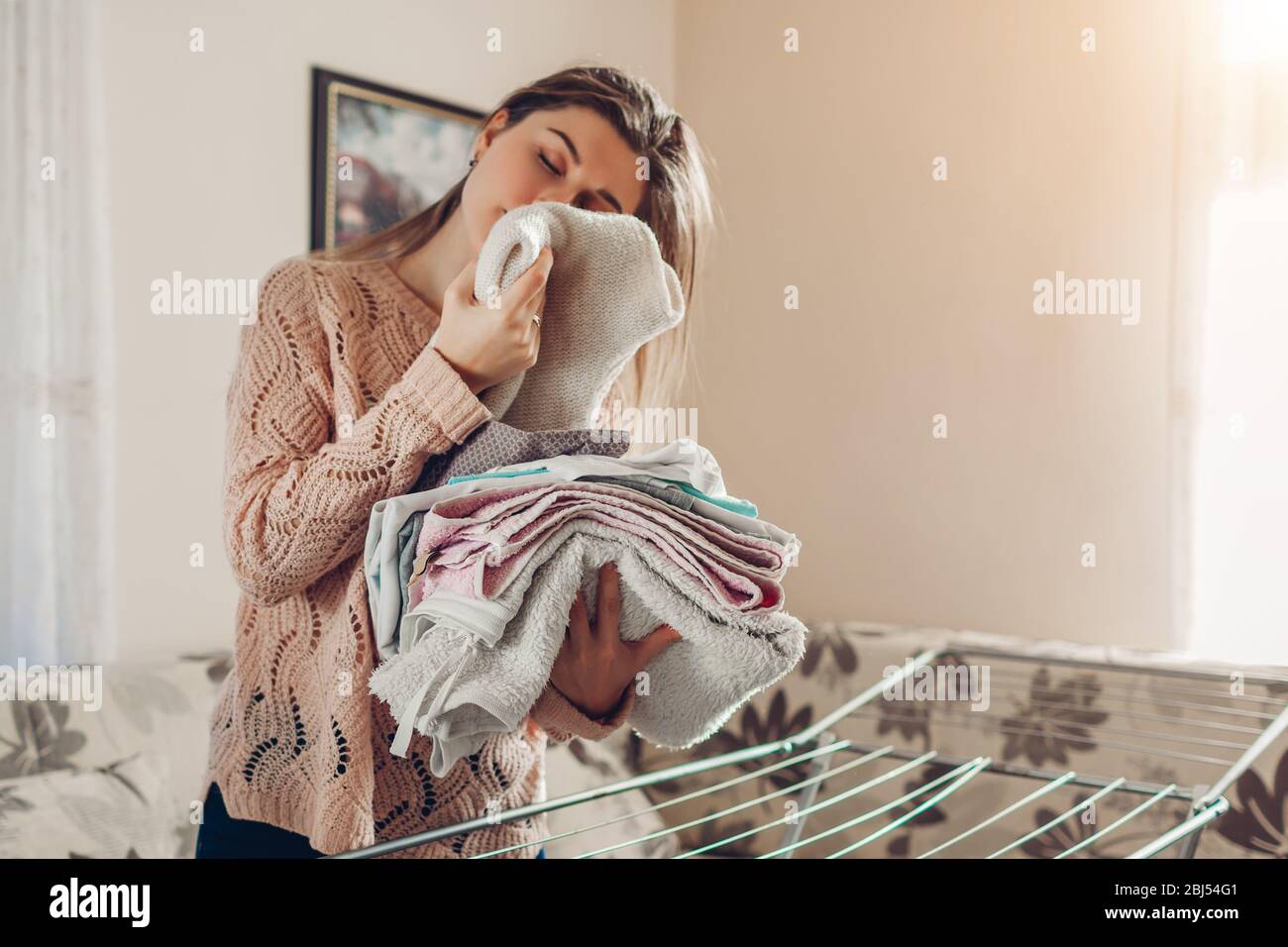 Happy woman smelling gathered clean clothes from dryer in heap
